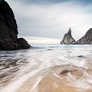 Ocean waves crashing on the sandy beach of Praia da Ursa surrounded by cliffs, Cabo da Roca