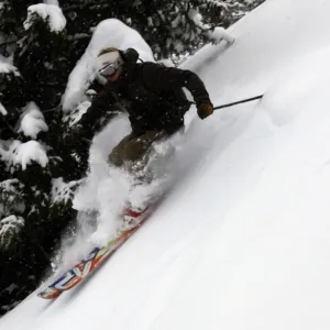 An off-piste skier in deep powder in the forests above Courmayeur and the east side of Mont Blanc