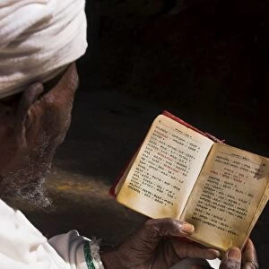 Old man wearing traditional gabi (white shawl) reading Holy Bible in rock-hewn monolithic church of Bet Medhane Alem (Saviour of the World), Lalibela