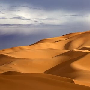 Orange sand dunes against stormy sky, Erg Chebbi sand sea, part of the Sahara Desert near Merzouga