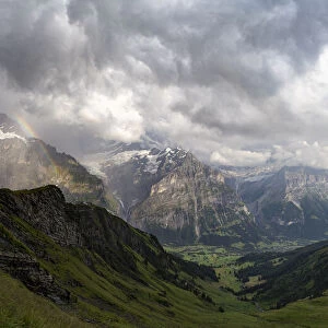 Panoramic of green valley surrounding Grindelwald and Bernese Alps lit by rainbow, First