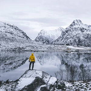 Person admiring the snowcapped mountains reflected in frozen sea, Flakstadpollen, Flakstadoya, Nordland, Lofoten Islands, Norway, Scandinavia, Europe