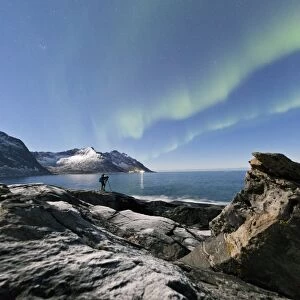 Photographer under the stars and Northern Lights (aurora borealis) surrounded by rocky peaks