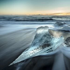 Pieces of glacier ice washed up on black volcanic sand beach at sunrise, near Jokulsarlon