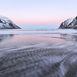 The pink light of sunrise over the waves of frozen sea surrounded by snowy peaks