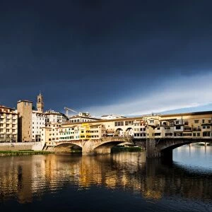 Ponte Vecchio reflecting in the Arno rRver against a dark blue stormy sky, Florence