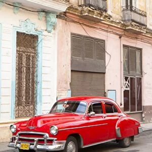 Restrored red American car pakred outside faded Colonial buildings, Havana