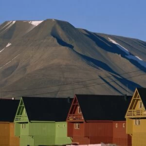 Row of painted wooden miners huts backed by grey mountain