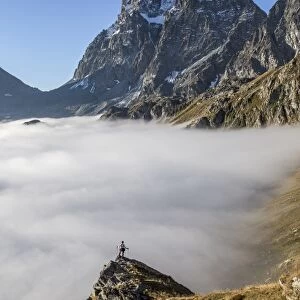 A solitary hiker admiring the profile of the Monviso (Monte Viso) emerging from the fog, Piedmont, Italy, Europe