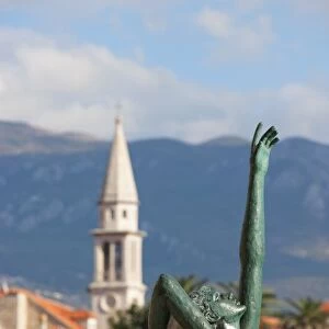 Statue of naked dancing girl on a rock with Budva old town in the background