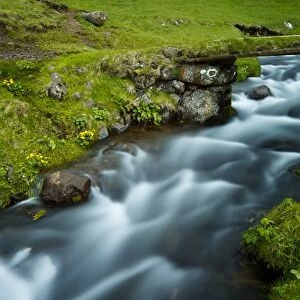 A stream running through the picturesque village of Gasadalur, which is overlooked by the 612m Heinanova mountain, Gasadalur, Vagar Island, Faroe Islands