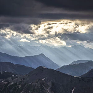 Sun rays filter between black clouds at sunset, Stelvio Mountain pass, Stelvio National Park, Valtellina, Lombardy, Italy, Europe