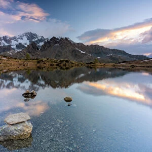 Sunrise lit the rocky peak of Monte Disgrazia mirrored in the clear water of lake Zana