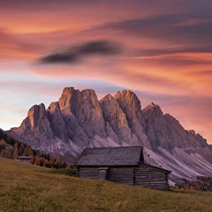 Sunrise over the Odle peaks and traditional hut in Gampen Alm in autumn, Funes Valley
