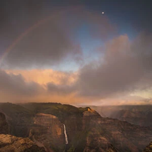 Sunset rainbow arches over the Waimea Canyon and Waipo o Falls towards the moon