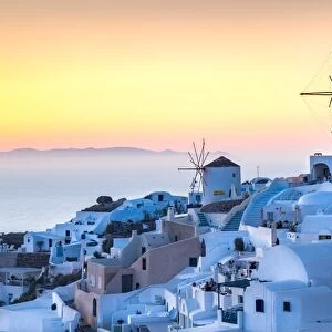 Sunset over the white stone buildings and windmills of Oia on the tip of Santorinis caldera