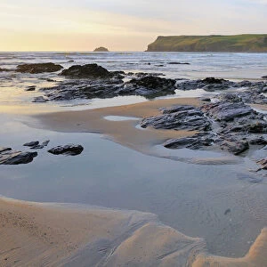 Tide retreating at sunset leaving tide pools among rocks, with Pentire Head in the background, Polzeath, Cornwall, England, United Kingdom, Europe
