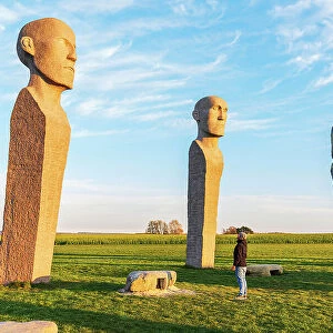 Tourist admiring Dodekalitten statues at sunset, Lolland island, Zealand region, Denmark, Europe