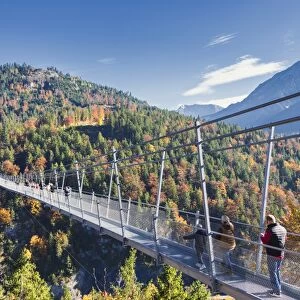 Tourists on the suspension bridge called Highline 179 framed by colorful woods in autumn