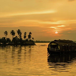 A traditional houseboat moves past the setting sun on the Kerala Backwaters, Kerala