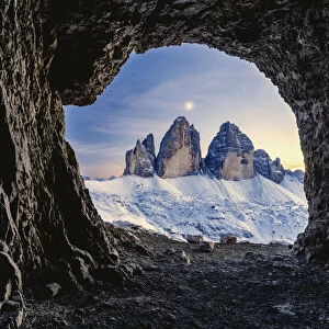 Tre Cime di Lavaredo lit by moon seen from opening in rocks of a war cave