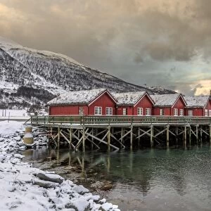 Typical red wooden huts of fishermen in the snowy and icy landscape of Lyngen Alps