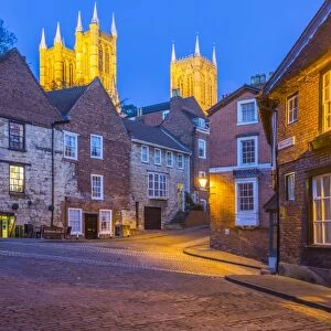 View of illuminated Lincoln Cathedral viewed from the cobbled Steep Hill at dusk