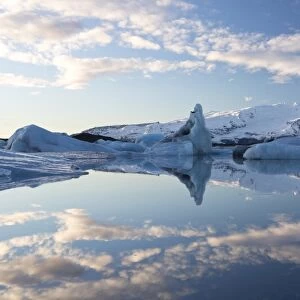 View over Jokulsarlon, a glacial lagoon at the head of the Breidamerkurjokull Glacier, towards icebergs and snow-capped mountains, with reflections in the calm water of the lagoon on a winters afternoon, on the edge of the Vatnajokull National Park, South Iceland, Iceland, Polar Regions