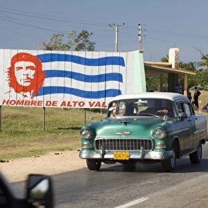 A vintage 1950s American Chevrolet on the road near Trinidad passing a colourful revolutionary road sign, Cuba, West Indies