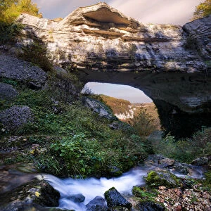 Waterfall flowing below Veja bridge, a huge natural arch in Lessinia, Veneto, Italy