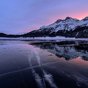 Winter sunrise on snowcapped mountains mirrored in the icy Lake Silvaplana, Maloja