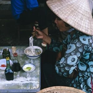 Woman eating pho (noodles) at food stall
