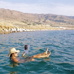 Woman floating in the Dead Sea reading a magazine