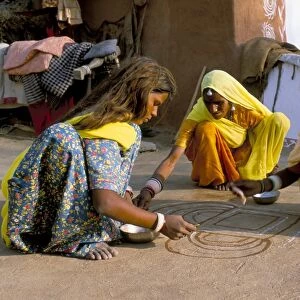 Women painting a mandana on the ground