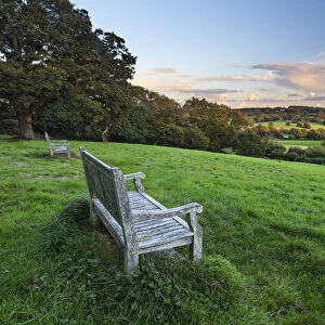 Wooden bench looking over green field countryside of High Weald on summer evening