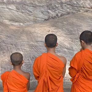 Three young monks praying at a rock-cut image of the