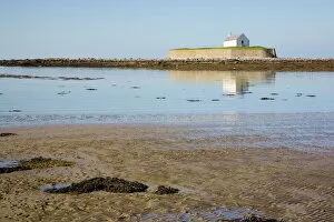 The 12th century Llangwyfan church on small tidal island reflected in calm sea