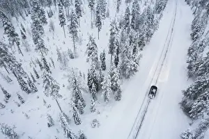 Finland Prints: Aerial view of a car driving through the snow covered forest on icy road