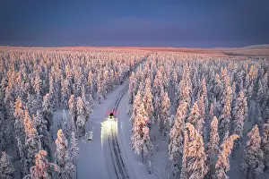 Akaslompolo Prints: Aerial view of car on icy road and illuminated headlamps driving in the snowcapped forest
