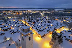 Aerial view of illuminated cottages and bell tower covered with snow in the old village of Gammelstad Church Town at dusk, UNESCO World Heritage Site, Lulea, Norrbotten, Norrland, Sweden, Scandinavia, Europe