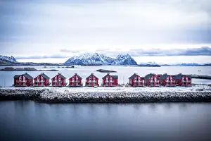 Svolvaer Prints: Aerial view of red rorbu cabins in a row amidst the cold sea in winter