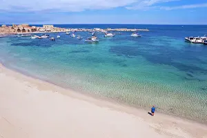 Mature Man Prints: Aerial view of tourist standing in an empty white sand beach looking at the sea in front of the fishing village of