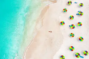 Antigua Prints: Aerial view of woman in bikini sunbathing on a tropical beach next to colorful umbrellas