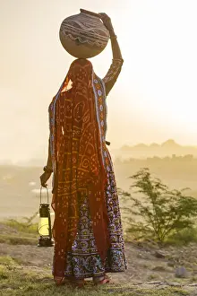 Adults Prints: Ahir Woman in traditional colorful cloth carrying water in a clay jug on her head