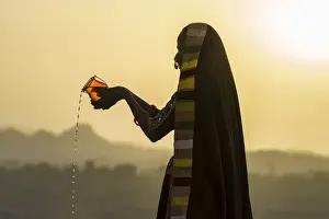 Headscarf Prints: Ahir Woman in traditional colorful cloth pouring water at sunset, Great Rann of Kutch