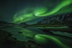 Aurora borealis (Northern Lights) reflected in partially frozen lake, North Snaefellsnes