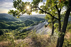 Badlands Prints: Badlands and green hills framed by trees and a sunburst, Emilia Romagna, Italy, Europe