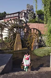 A Bai girl carrying buckets of water in front of a water wheel in Lijiang Old Town