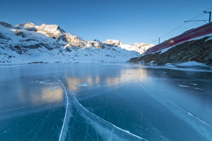 The Bernina Express train runs beside the frozen Lago Bianco, Bernina Pass, canton of Graubunden
