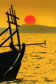 Silhouettes Prints: Big red setting sun beyond fishing boat moored off beach south of the city, Otres Beach